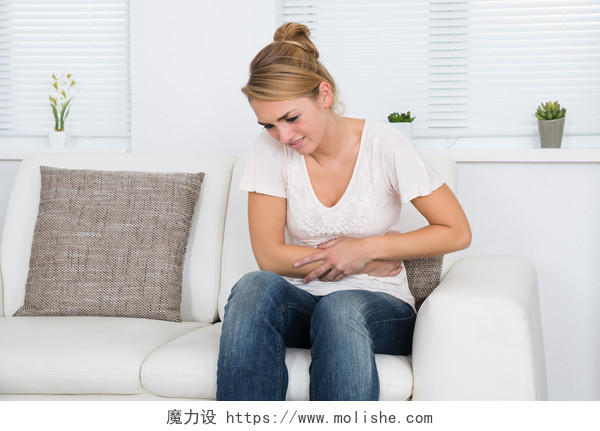女性双手捂着肚子坐在沙发上难受女生痛经肚子痛